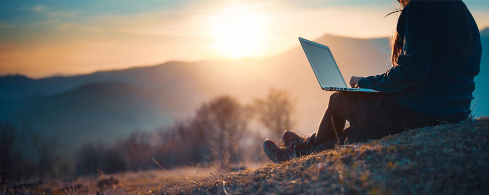 En kvinna sitter med en dator i naturen